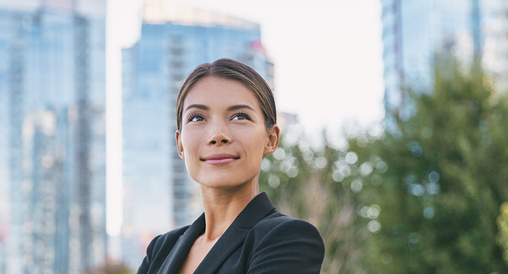 Inspired businesswoman looking up towards tall city buildings