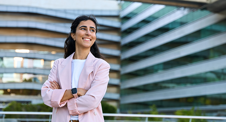 Confident young business woman smiling and standing in front of tall buildings